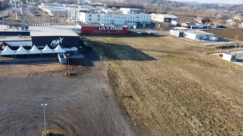 Luftbild eines großen unbebauten Grundstücks neben Gewerbegebäuden und einem Einkaufszentrum.