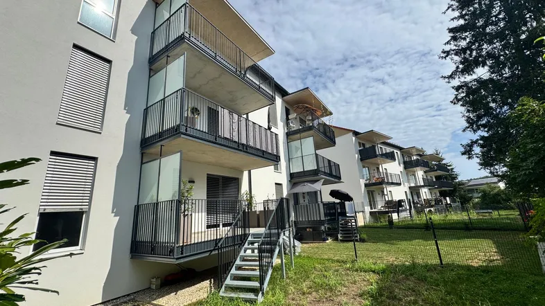 Moderne Wohnanlage mit mehreren Balkonen und Terrassen, umgeben von Grünflächen unter blauem Himmel.