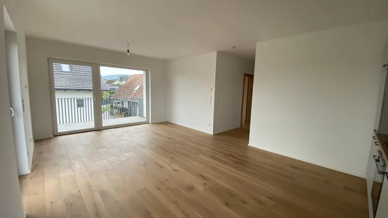 Heller Wohnbereich mit Holzboden und großen Fenstern, die viel Tageslicht hereinlassen.