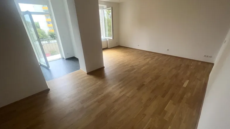 Helles Wohnzimmer mit Parkettboden und Zugang zu einem kleinen Balkon.