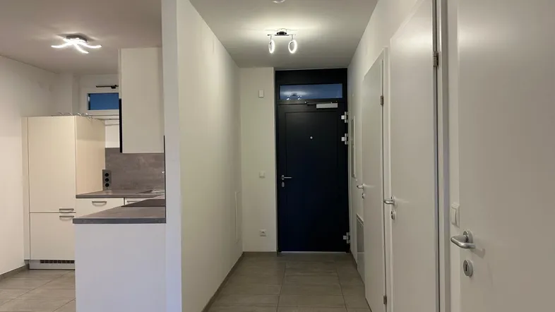 Heller Flur mit Zugang zur Küche und zur Eingangstür, ausgestattet mit modernen Deckenleuchten.