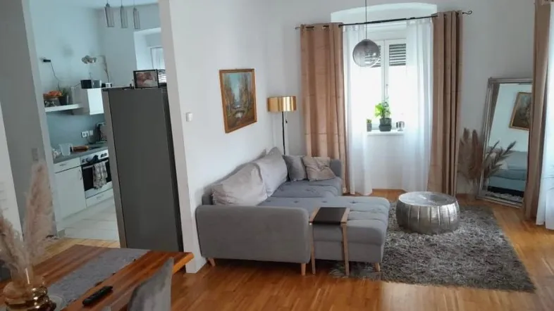 Helles Wohnzimmer mit gemütlichem Sofa, Holzboden und offenem Übergang zum Essbereich und zur Küche.