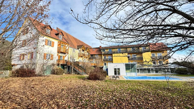 Gebäudeansicht mit Außenpool, umgeben von herbstlichem Laub und Bäumen unter blauem Himmel.