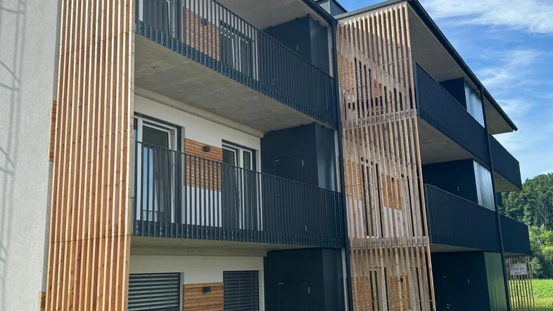 Moderne Wohnanlage mit Holzlamellenfassade und Balkonen unter blauem Himmel.