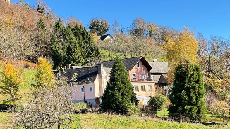 Mehrere Gebäude in einer ländlichen Umgebung mit Herbstbäumen und einem Kirchturm im Hintergrund.