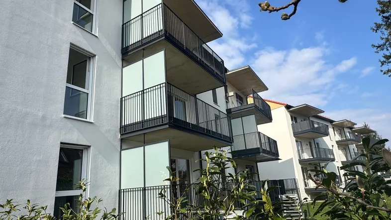 Moderne Wohngebäude mit mehreren Balkonen und weißer Fassade unter blauem Himmel.