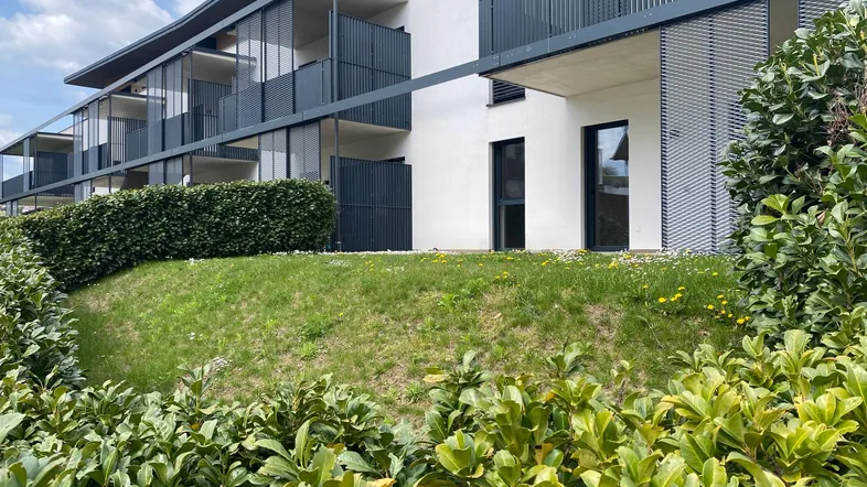 Moderne Wohnanlage mit weißer Fassade, Balkonen und gepflegter Hecke im Vordergrund.