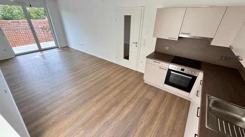 Offener Wohnbereich mit Laminatboden, Zugang zur Terrasse und integrierter Küchenzeile.
