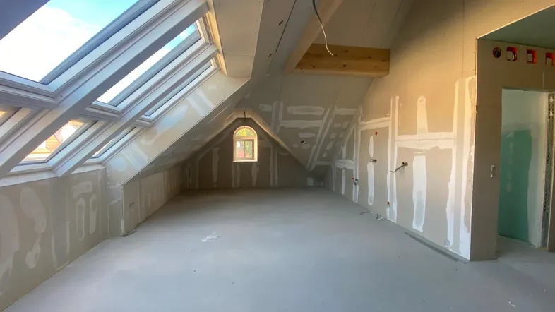 Geräumiger Dachbodenraum im Rohbau mit vielen Dachfenstern und natürlichem Lichteinfall.