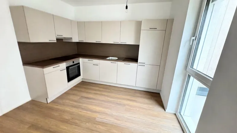 Moderne, helle Küche mit beigen Schränken, dunkler Arbeitsplatte und Laminatboden, bereit zur Nutzung.