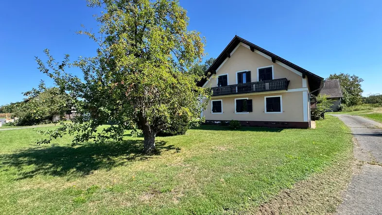 Haus mit Garten und Apfelbaum unter blauem Himmel in ländlicher Umgebung.