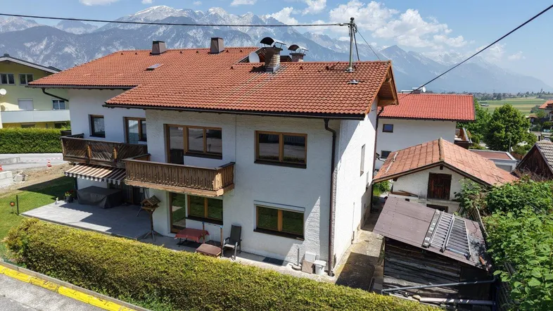 Gesamtansicht des Hauses mit rotem Ziegeldach und beeindruckendem Bergpanorama im Hintergrund.