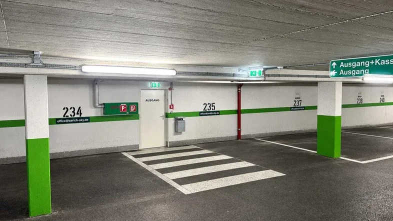 Tiefgarage mit markierten Parkplätzen, Betonwänden und Deckenbeleuchtung.