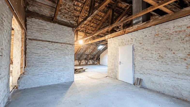 Geräumiger Dachboden mit freiliegenden Holzbalken, Ziegelwänden und einem Dachfenster, ideal für den Ausbau.