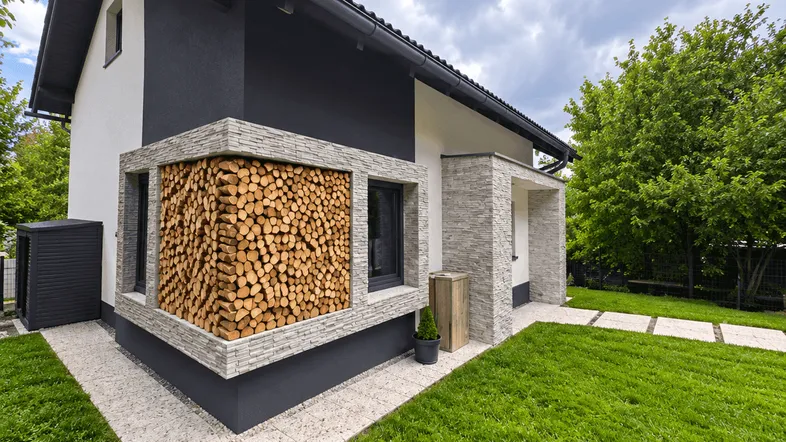 Modernes Einfamilienhaus mit dunkler Fassade, Holzstapel-Dekoration und gepflegtem Vorgarten.