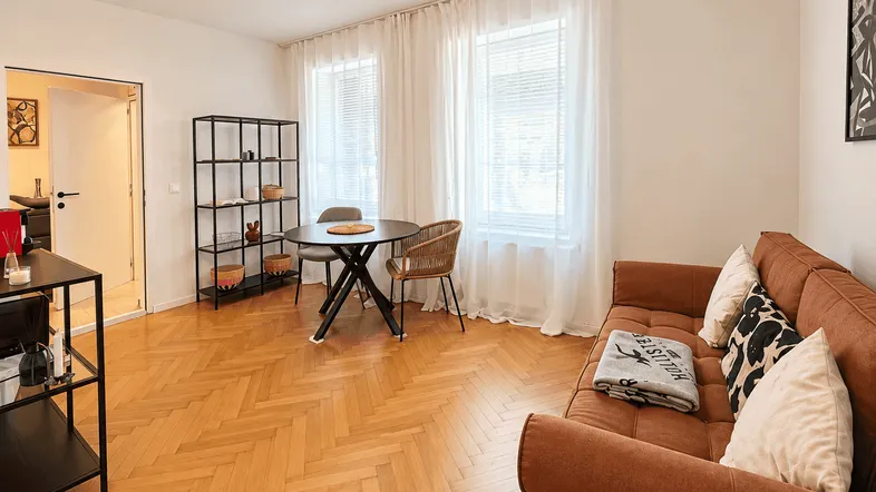 Helles Wohn- und Esszimmer mit Fischgrätparkett, bequemer Couch und kleinem Esstisch.