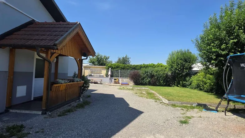 Weitläufiger Gartenbereich mit Kiesauffahrt, Rasenfläche und überdachtem Hauseingang.