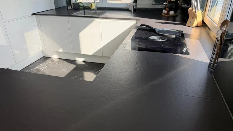 Moderne Küche mit schwarzen Arbeitsplatten, weißen Hochglanzschränken und Induktionskochfeld.