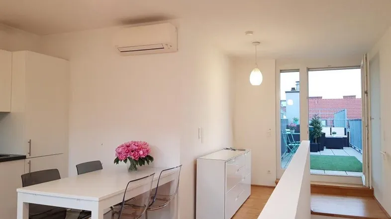Heller offener Wohnbereich mit Esstisch, moderner Küche und Zugang zu einer Dachterrasse.