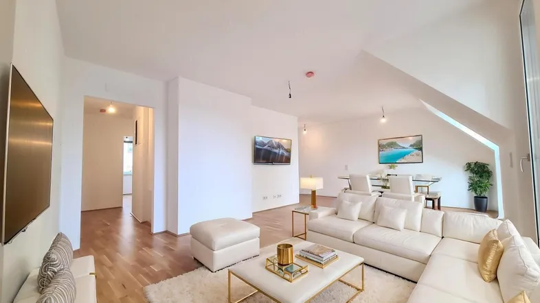 Helles, modern eingerichtetes Wohn-Esszimmer mit bequemer Couch, Holzboden und Dachschrägen.