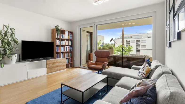 Helles Wohnzimmer mit Holzboden, modernem Sofa und Zugang zu einem sonnigen Balkon.