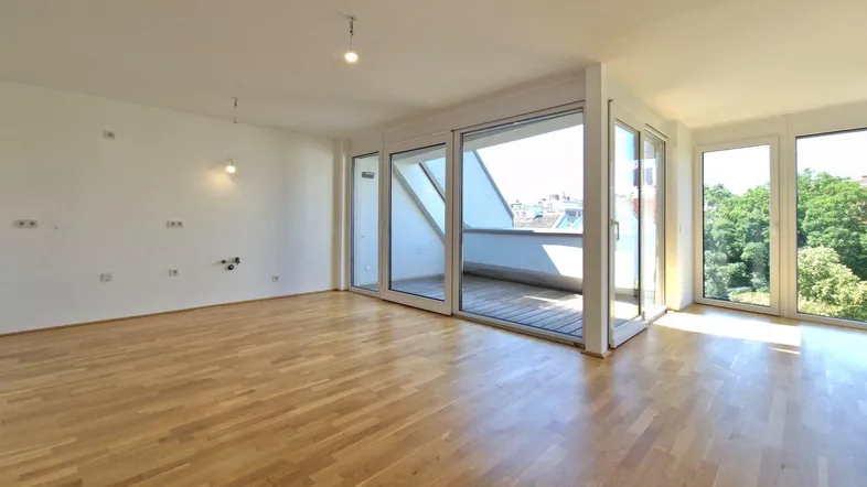 Helles, leeres Wohnzimmer mit Parkettboden und großen Fenstern, die Zugang zu einem Balkon bieten.