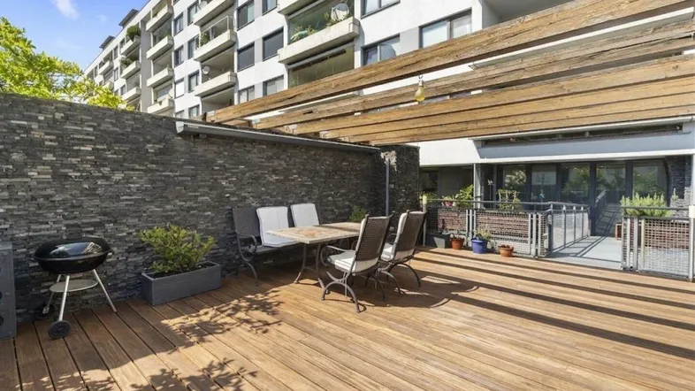 Geräumige Terrasse mit Holzdeck, Steinfassade und Grillbereich, ideal für entspannte Stunden im Freien.
