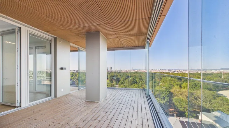 Geräumige Terrasse mit Holzboden, Glasgeländer und weitem Blick über die Stadt und Grünflächen.