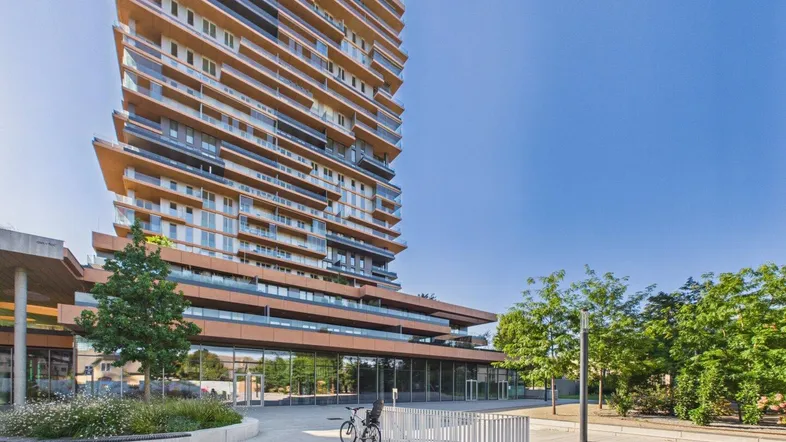 Modernes Hochhaus mit vielen Balkonen und Glasfassade in urbaner Umgebung.
