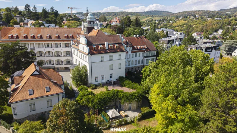 Luftaufnahme eines historischen Gebäudekomplexes mit umliegender grüner Landschaft und Weinbergen.