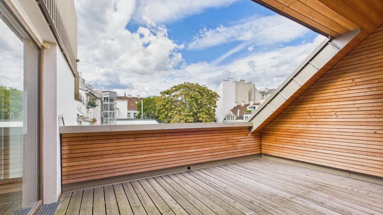 Geräumige Dachterrasse mit Holzboden und Blick auf die umliegende Stadtlandschaft unter blauem Himmel.