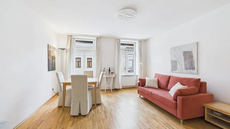Helles Wohn- und Esszimmer mit Parkettboden, rotem Sofa und Blick auf die Straße.