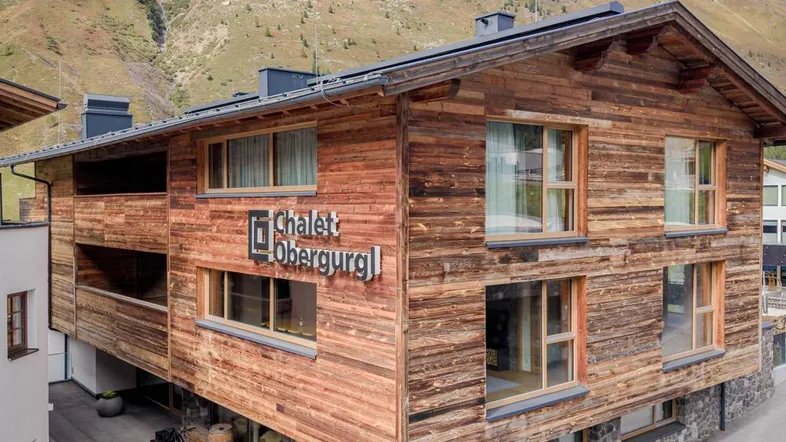 Modernes Chalet mit Holzfassade und großen Fenstern, eingebettet in eine alpine Berglandschaft.