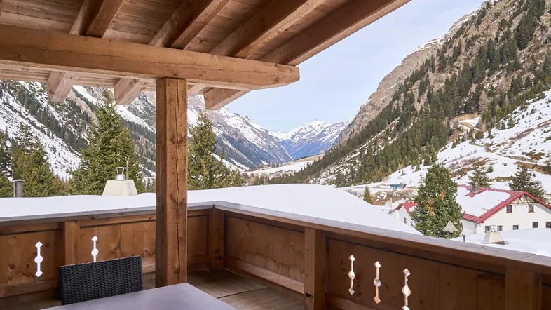 Überdachter Holzbalkon mit Sitzgelegenheiten und atemberaubendem Blick auf die verschneiten Berge.