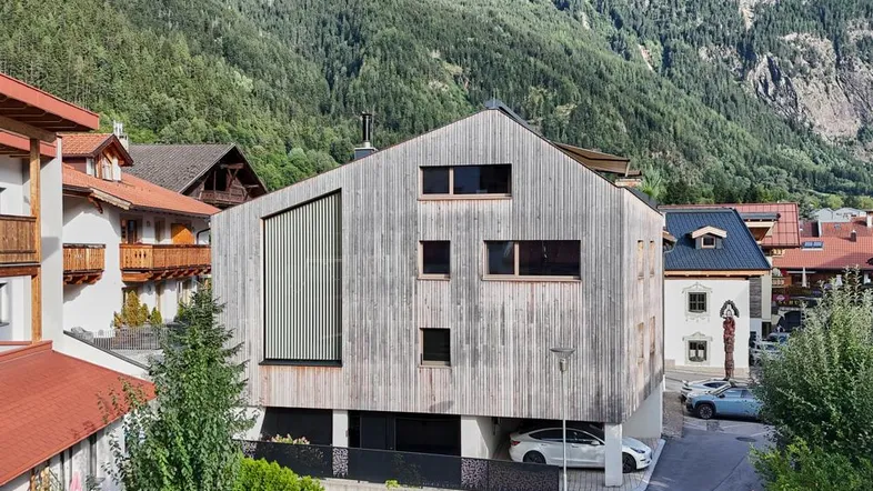 Moderne Holzfassade eines Hauses in alpiner Umgebung mit Bergblick und integriertem Carport.