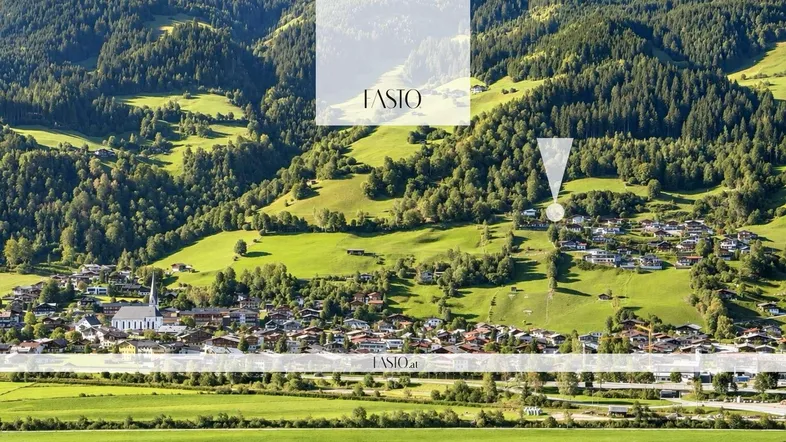 Luftaufnahme eines malerischen Dorfes in einem grünen Tal, umgeben von bewaldeten Bergen.