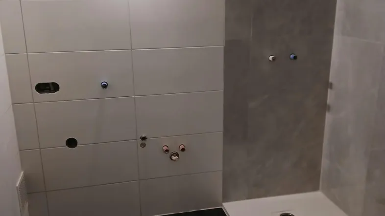 Badezimmer im Bau mit grauen Fliesen, Duschwanne und sichtbaren Installationen.