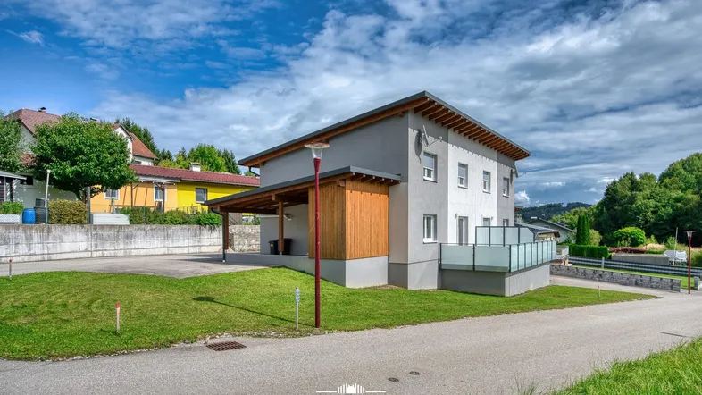 Modernes Mehrfamilienhaus mit heller Fassade, Holzverkleidung und Carport in ländlicher Umgebung.