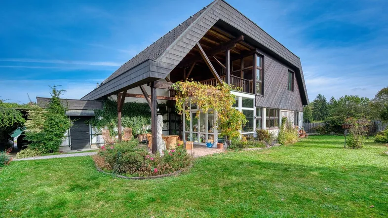 Haus mit großem Garten und überdachter Terrasse unter blauem Himmel.