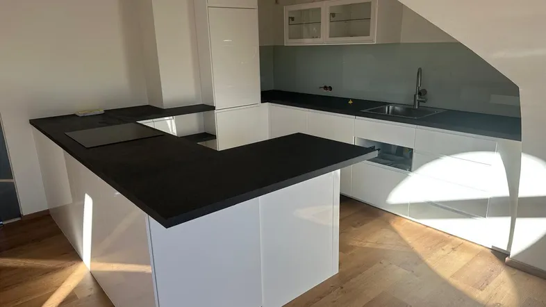 Moderne Küche mit weißen Hochglanzfronten, dunkler Arbeitsplatte, Induktionskochfeld und Dachschräge.