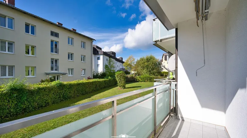Heller Balkon mit Blick auf die grüne Gemeinschaftsfläche und umliegende Wohngebäude.