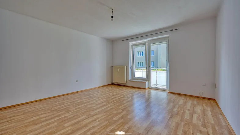 Heller, leerer Raum mit Laminatboden und Zugang zum Balkon, ideal als Wohnzimmer.