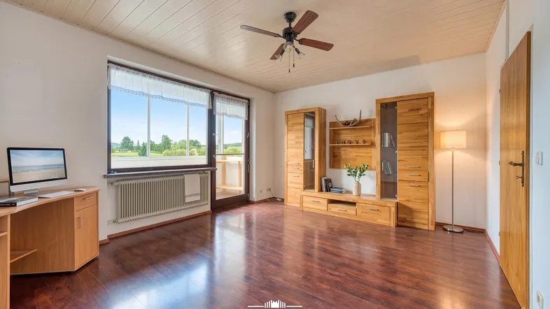 Helles Wohnzimmer mit dunklem Laminatboden, Holzmöbeln und Zugang zu einem Balkon.