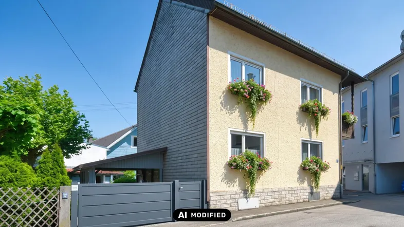 Einfamilienhaus mit heller Fassade, Blumenkästen an den Fenstern und einem modernen grauen Tor.
