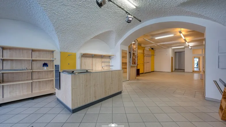 Geräumiger Ladenbereich mit gewölbter Decke, Fliesenboden und Holzregalen, bereit für die Einrichtung.