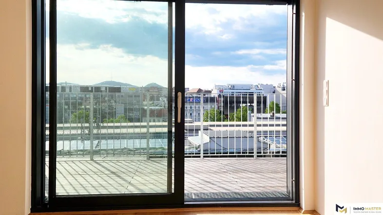Heller Innenraum mit großen Schiebetüren, die auf eine Terrasse mit Stadtblick führen.