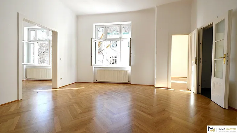 Helles Zimmer mit Fischgrätparkettboden und großen Fenstern, das viel Tageslicht hereinlässt.