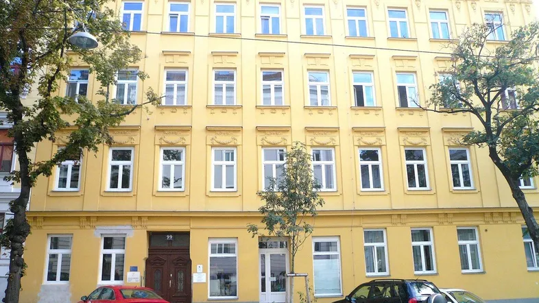 Historisches Gebäude mit gelber Fassade, vielen Fenstern und dekorativen Elementen unter dem Dach.