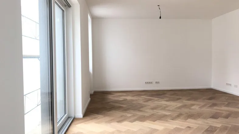 Helles Zimmer mit Fischgrätparkett und Zugang zu einem Balkon oder einer Terrasse.