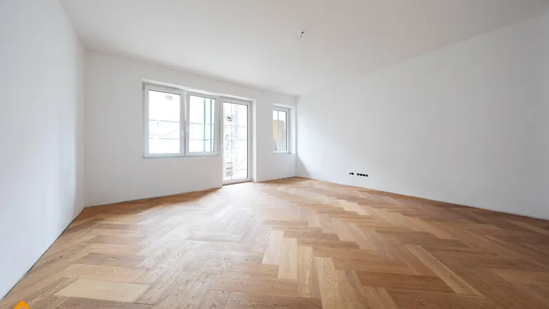 Helles Zimmer mit Fischgrätparkett und Zugang zu einem Balkon oder einer Terrasse.